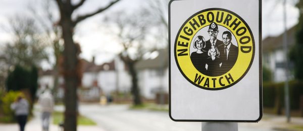A yellow and black Neighbourhood watch sign displayed on a signpost in a tree lined road