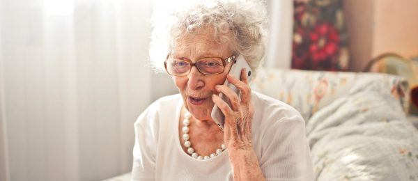 Elderly lady is smiling whilst talking on the phone whilst sitting in an armchair at home