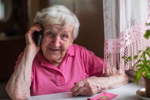 Elderly woman talks on a mobile phone sitting at home, looking happy and smiling
