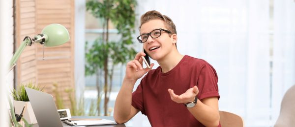 Smiling young man sat at desk talking into telephone