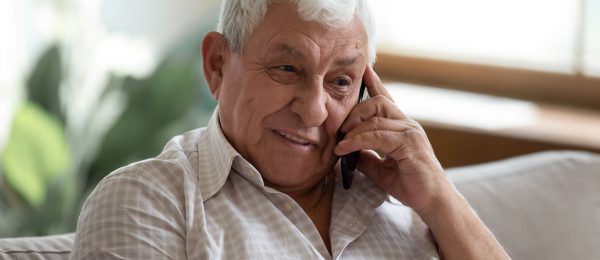 A senior man sits on sofa in living room talking on the telephone