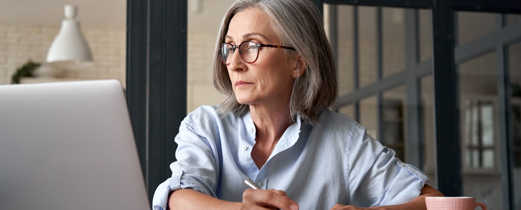 middle aged businesswoman taking notes while using computer technology sitting at a table