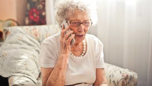 An elderly woman chats happily on the telephone whilst sitting in an armchair