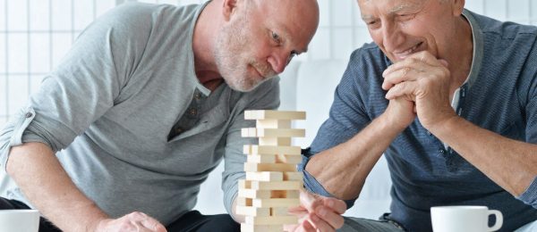 2 men sit across a table playing Jenga , a game where a tower of bricks is dissembled.